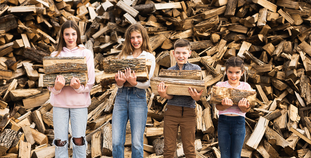 The four kids of Durham Firewood loaded up with logs and firewood in front of a giant pile of firewood